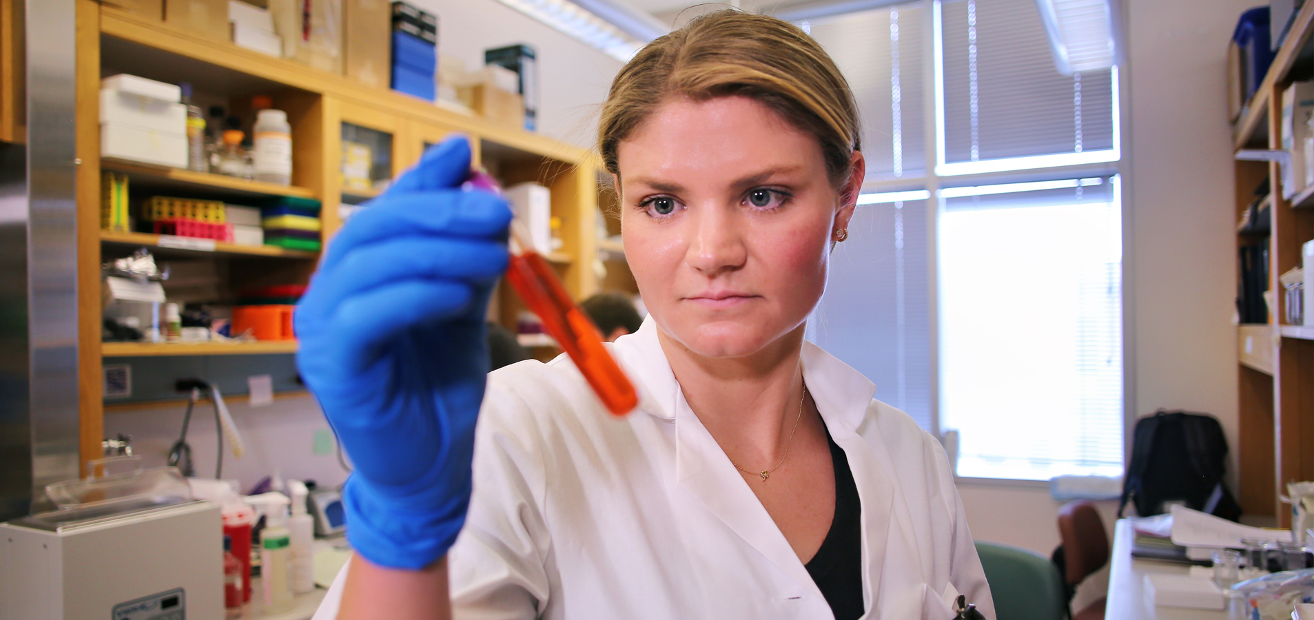 A female School of Nursing Student doing Research in a lab holding a test tube with red liquid.