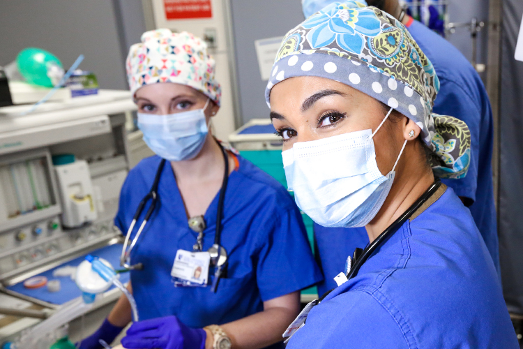 Two Duke CRNA Nurse Anesthesia Students in a simulated operating room environment wearing blue scrubs and masks. 