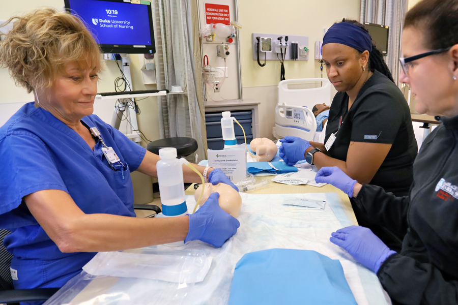 Duke University MSN Neonatal Nurse Practitioner faculty leading a neonatal delivery simulation. Two Duke NNP Nursing students watch carefully before attempting the simulation procedure. themselves. 