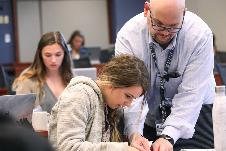 A male Duke University School of Nursing leading faculty member, Dr. Allen Cadavero guides an MSN education student in a large classroom setting.