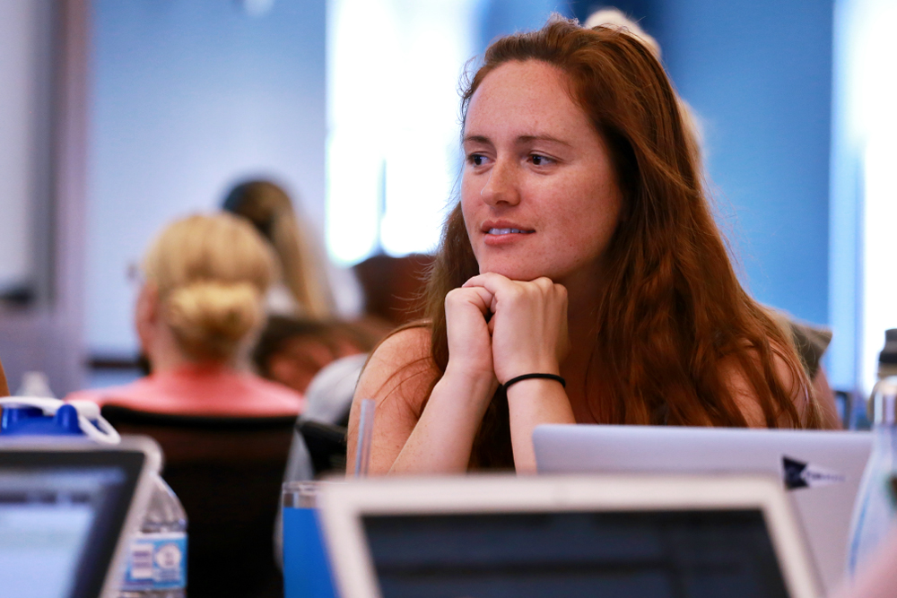 A female Duke University School of Nursing MSN Health Informatics student has her hands under her chin and looks thoughtful among other students in a large classroom setting.  