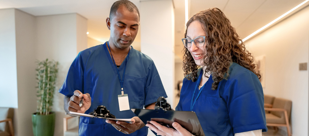 Two nurses talking in a hallway looking at a clipboard