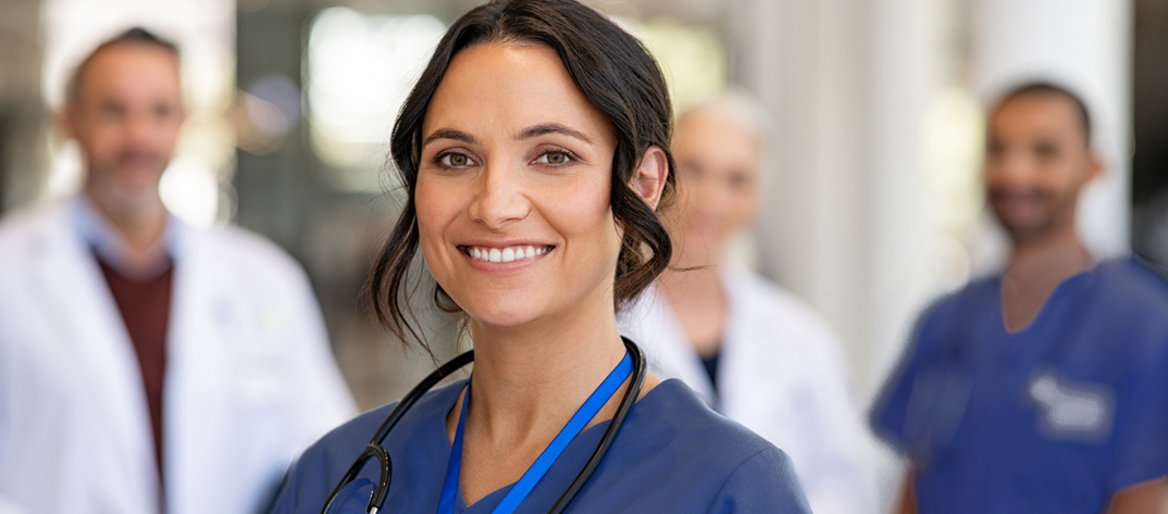 Nurse smiling in foreground with other staff behind her