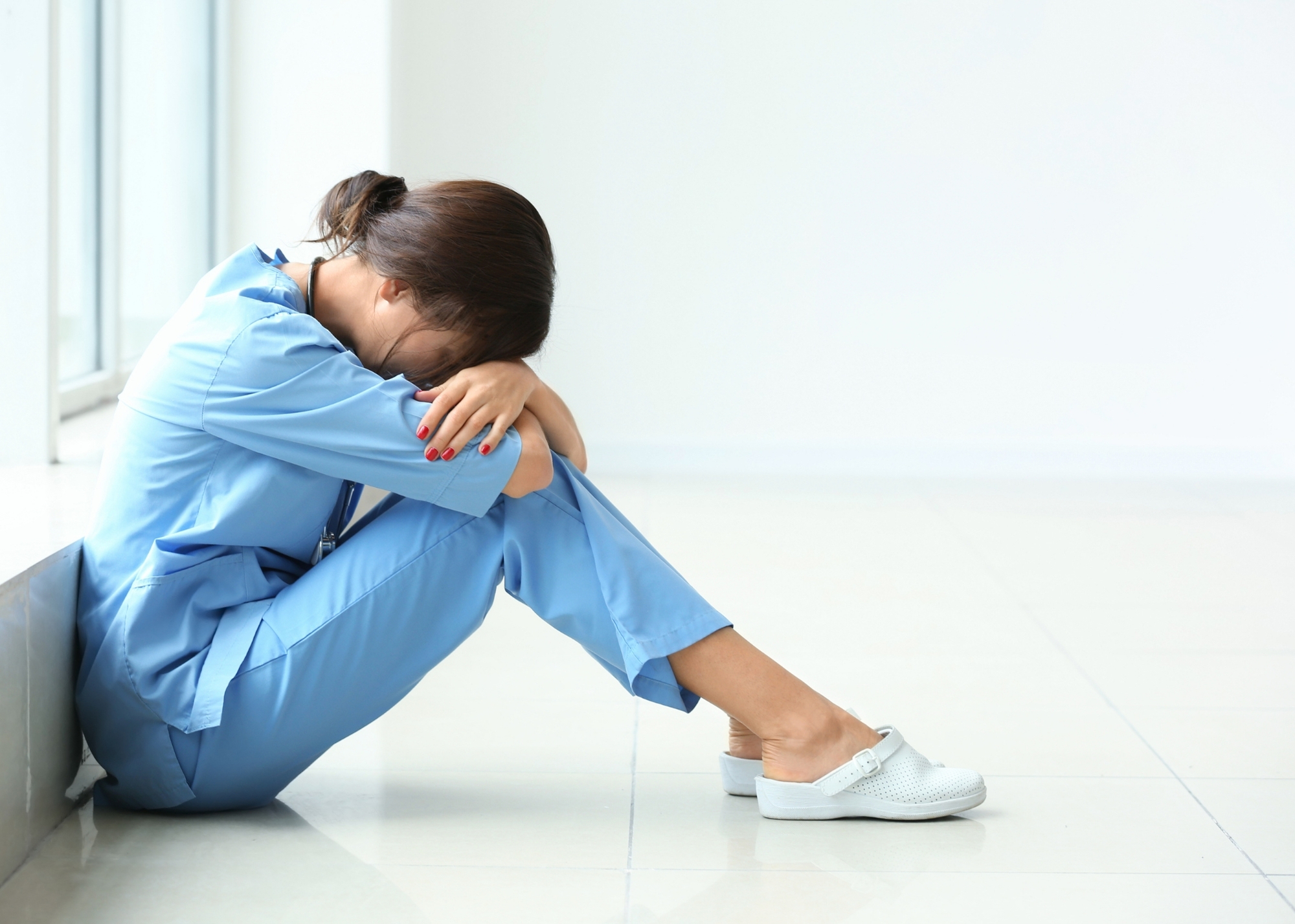 A nurse sitting on the floor with her head in her hands