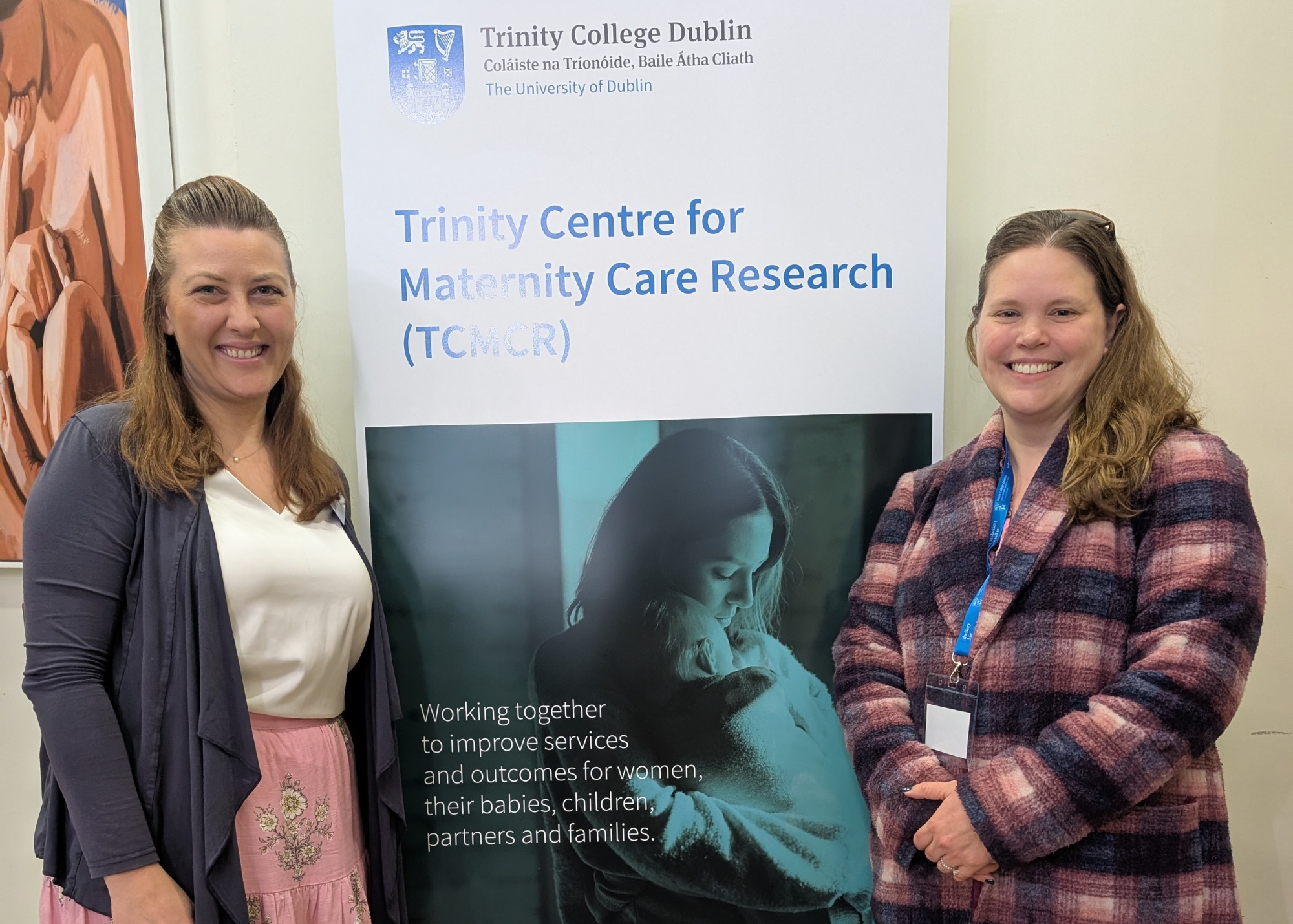 Bonnie Hepler and Kristin Tully stand beside a poster for Trinity College Dublin's Centre for Maternity Care Research