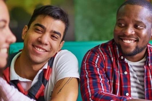 Three seated college-aged students smiling at each other, as if they'd just heard good news or something funny