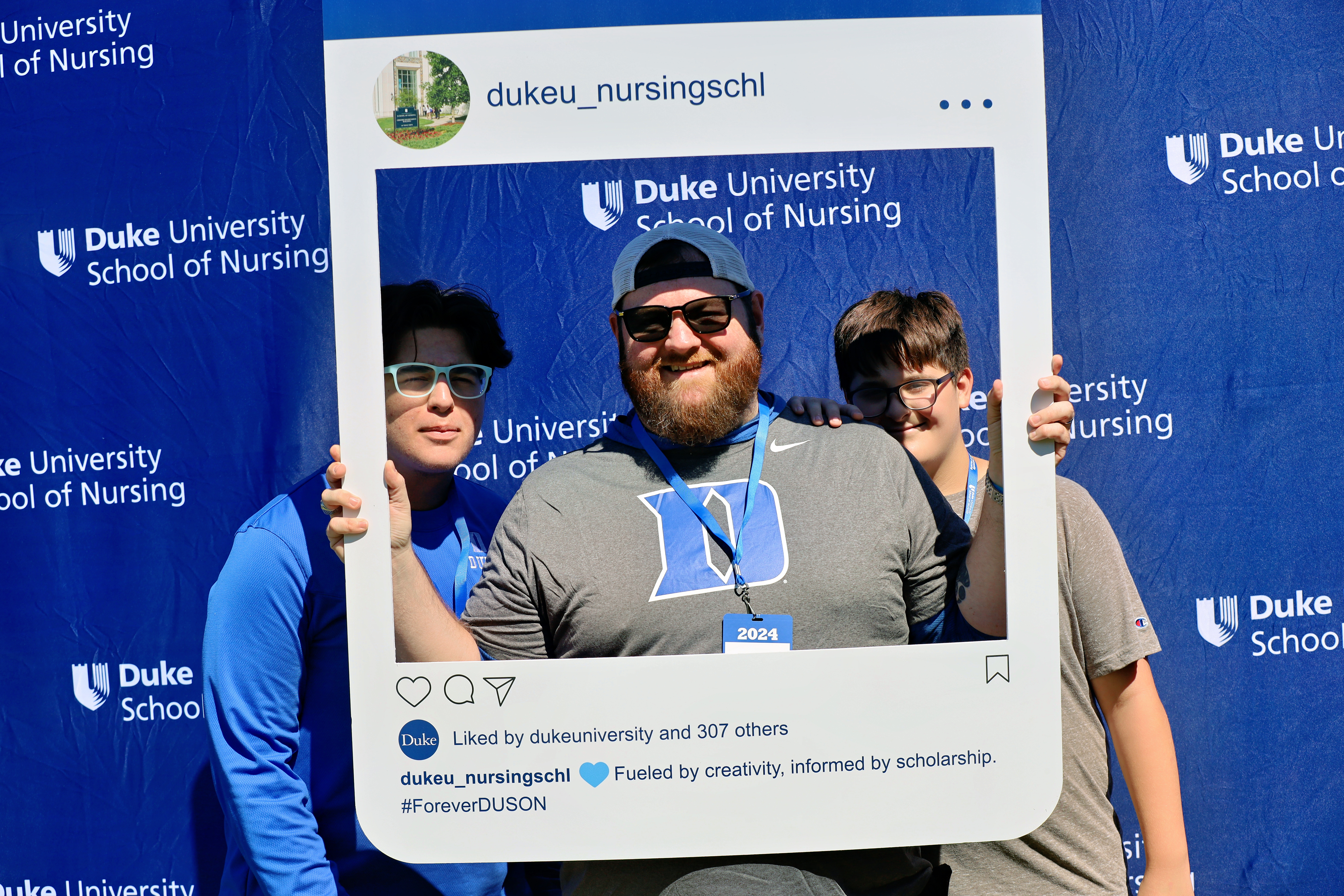 Duke School of Nursing alumni pose for photo with an large Instagram cutout frame during a Duke football tailgate.