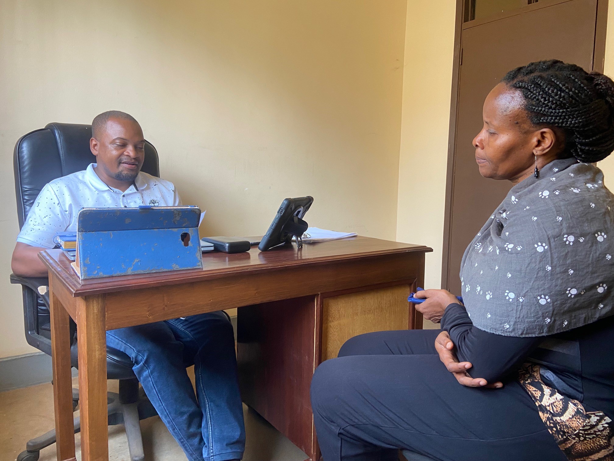 A man sits behind a desk with an iPad and a woman sits across from him