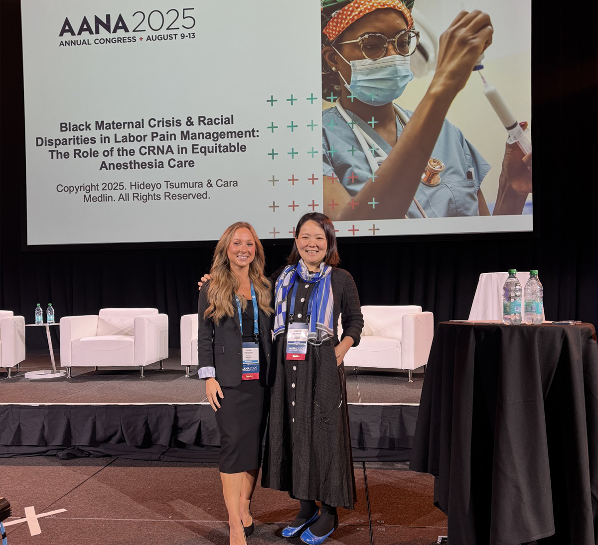 A student poses on stage at a conference, her presentation on the screen behind her.