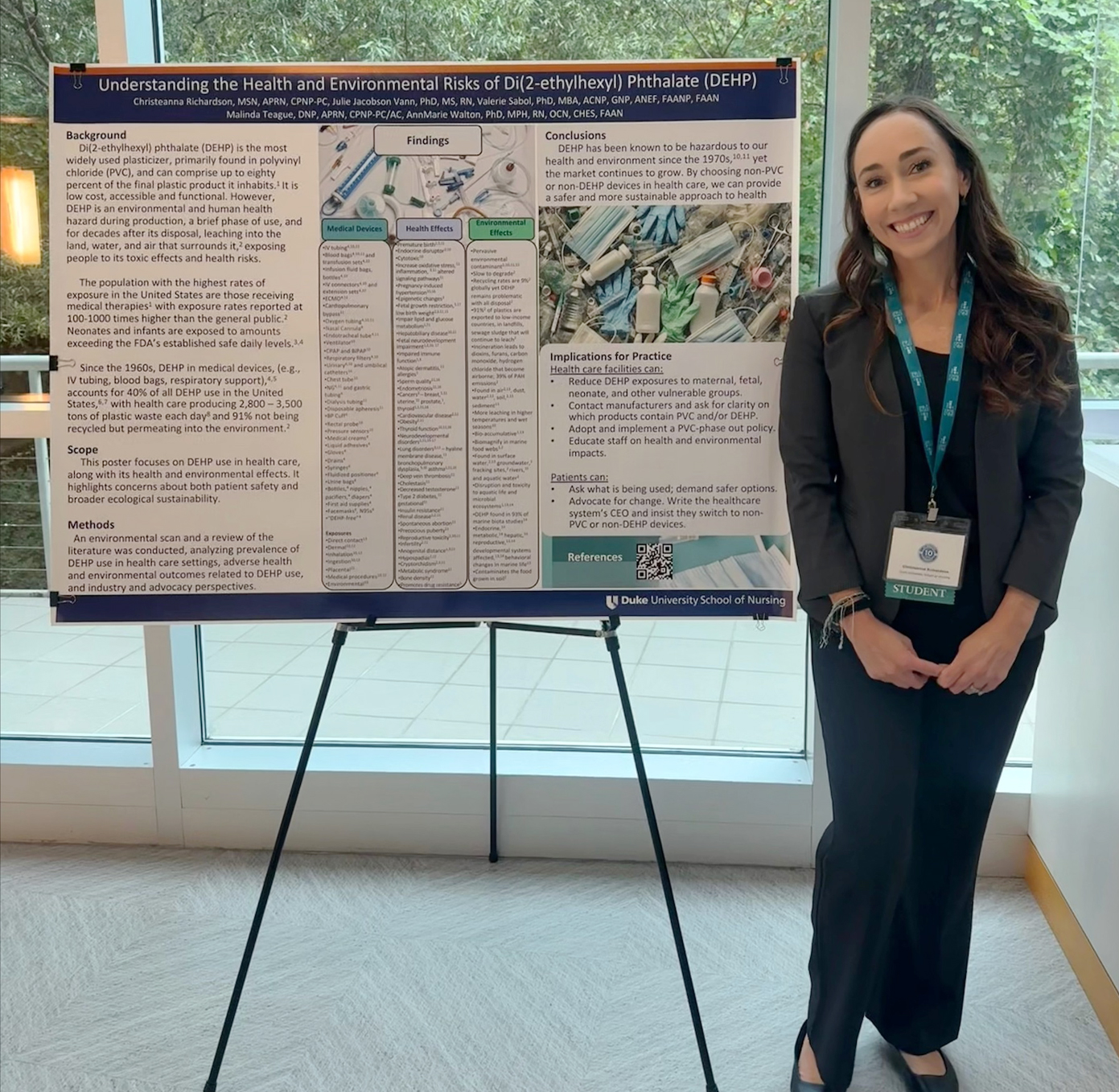 A student poses next to a poster on a tripod at a conference.