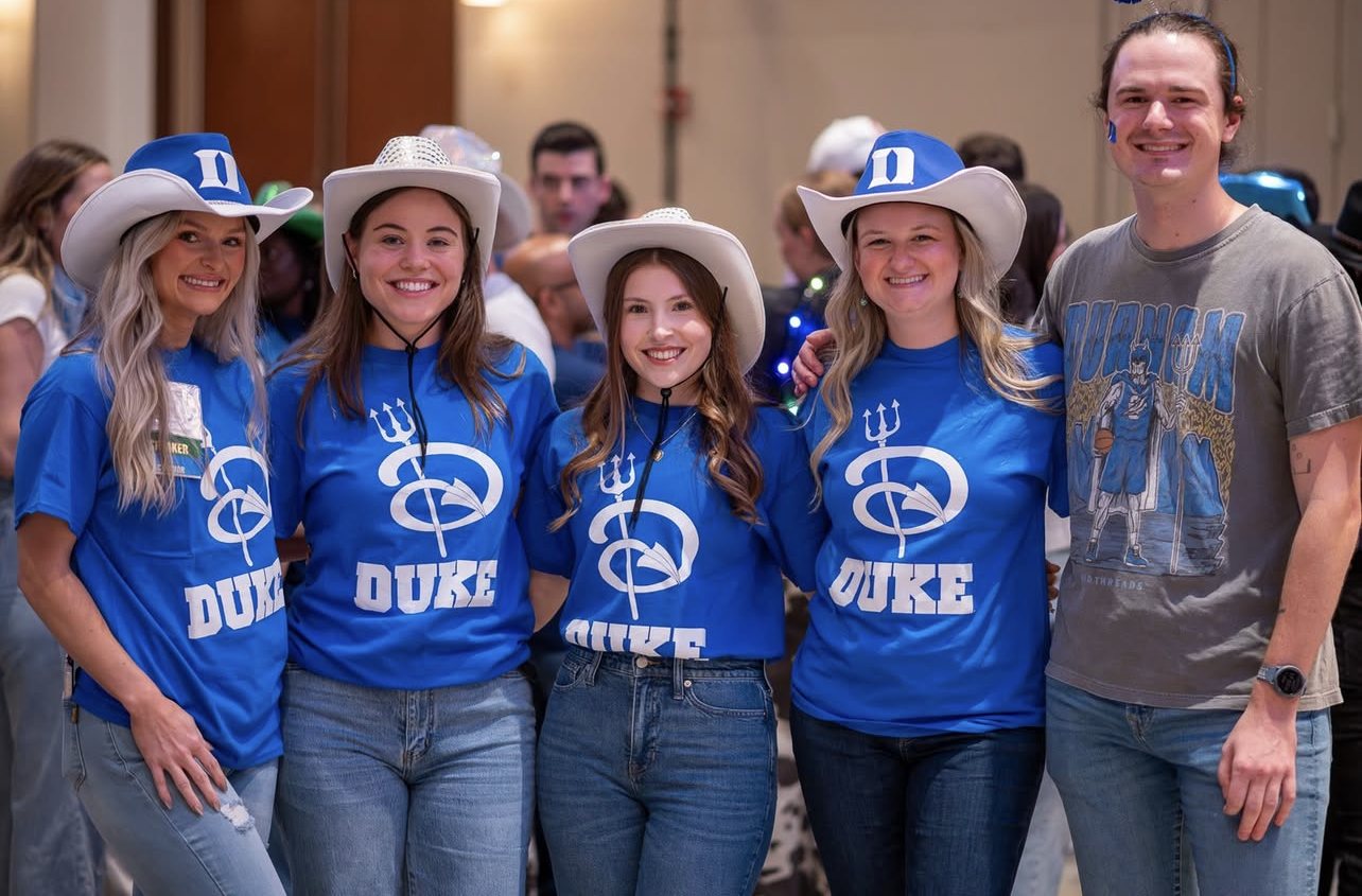 A group of students in Duke t-shirts and cowboy hats pose in a conference room.