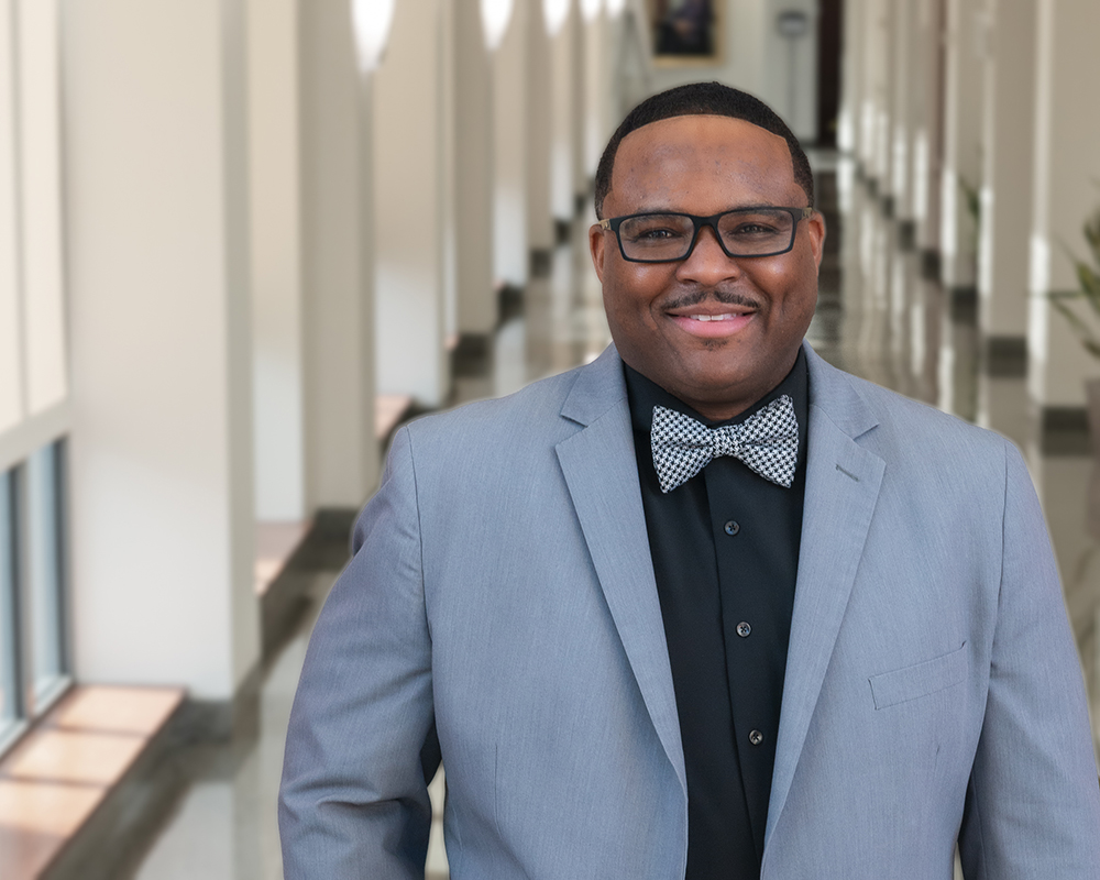 Dr. Michael Cary stands in a sunlit hallway smiling