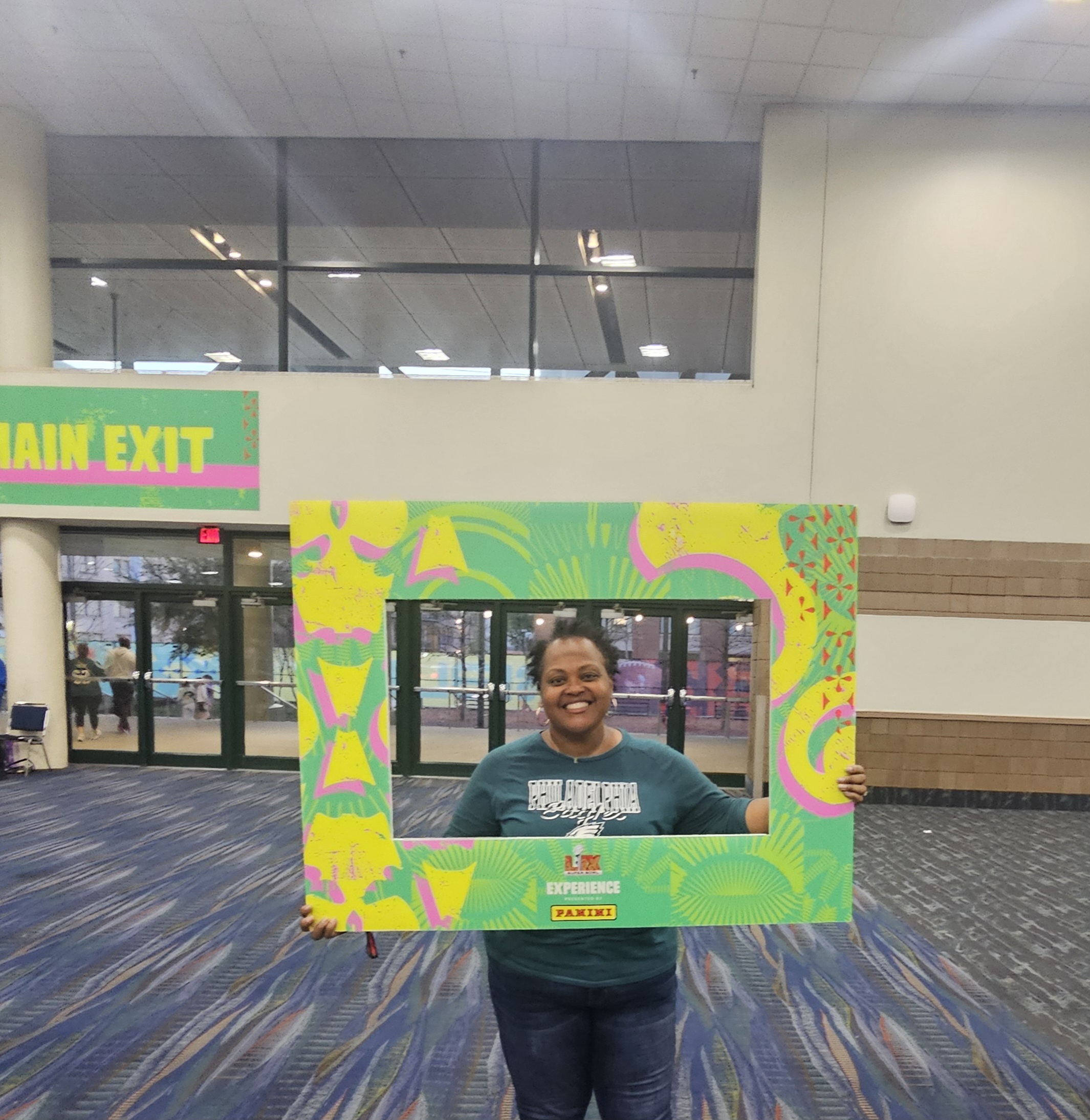 A person stands in front of a cut out frame in a large conference room.