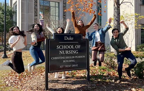 Duke School of Nursing Students jumping next to a sign