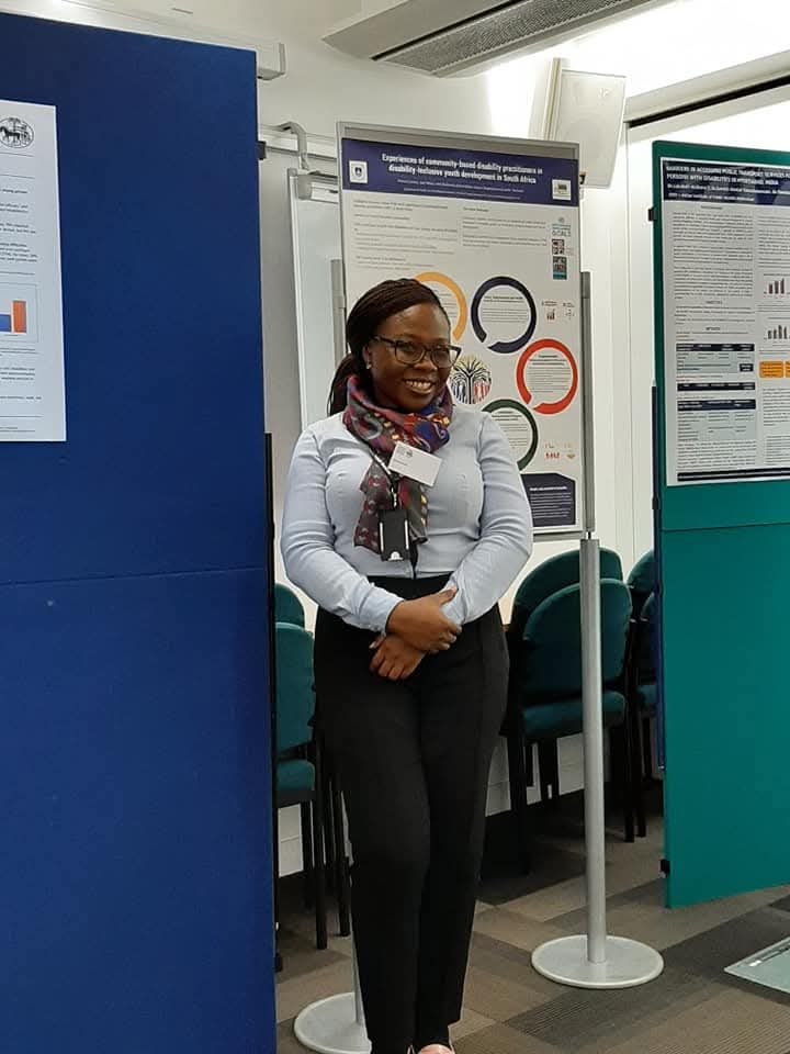 A woman in business casual stands in front of a poster as part of a poster presentation at a conference.