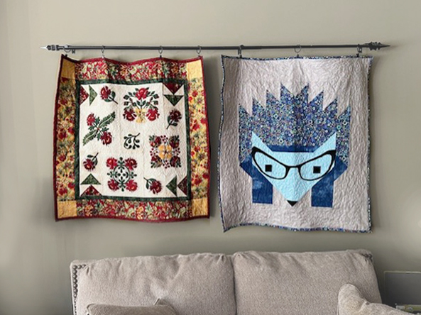 Two quilts hanging from a rod above a couch