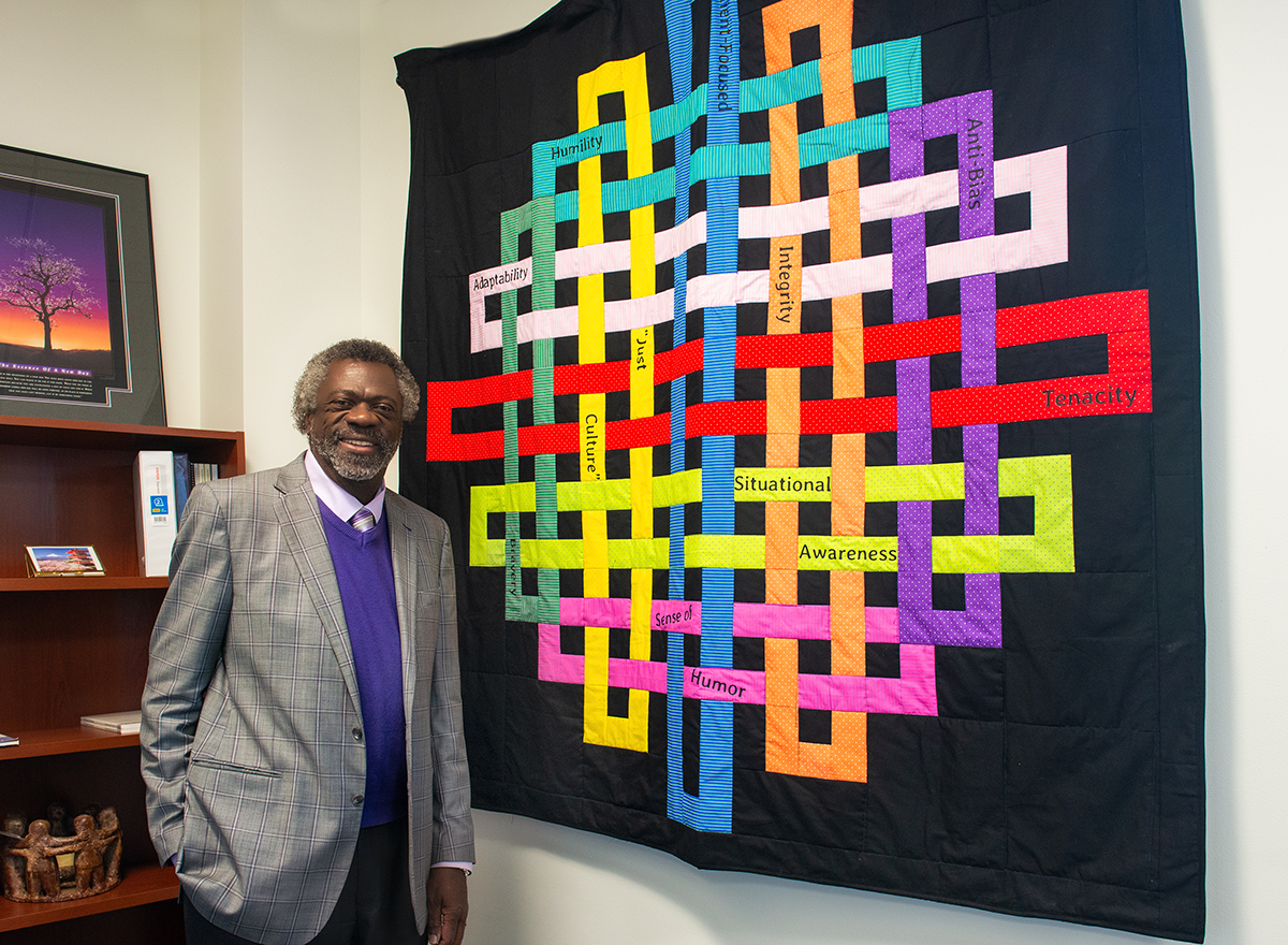 Dr. Grant standing beside the student-gifted quilt in his office