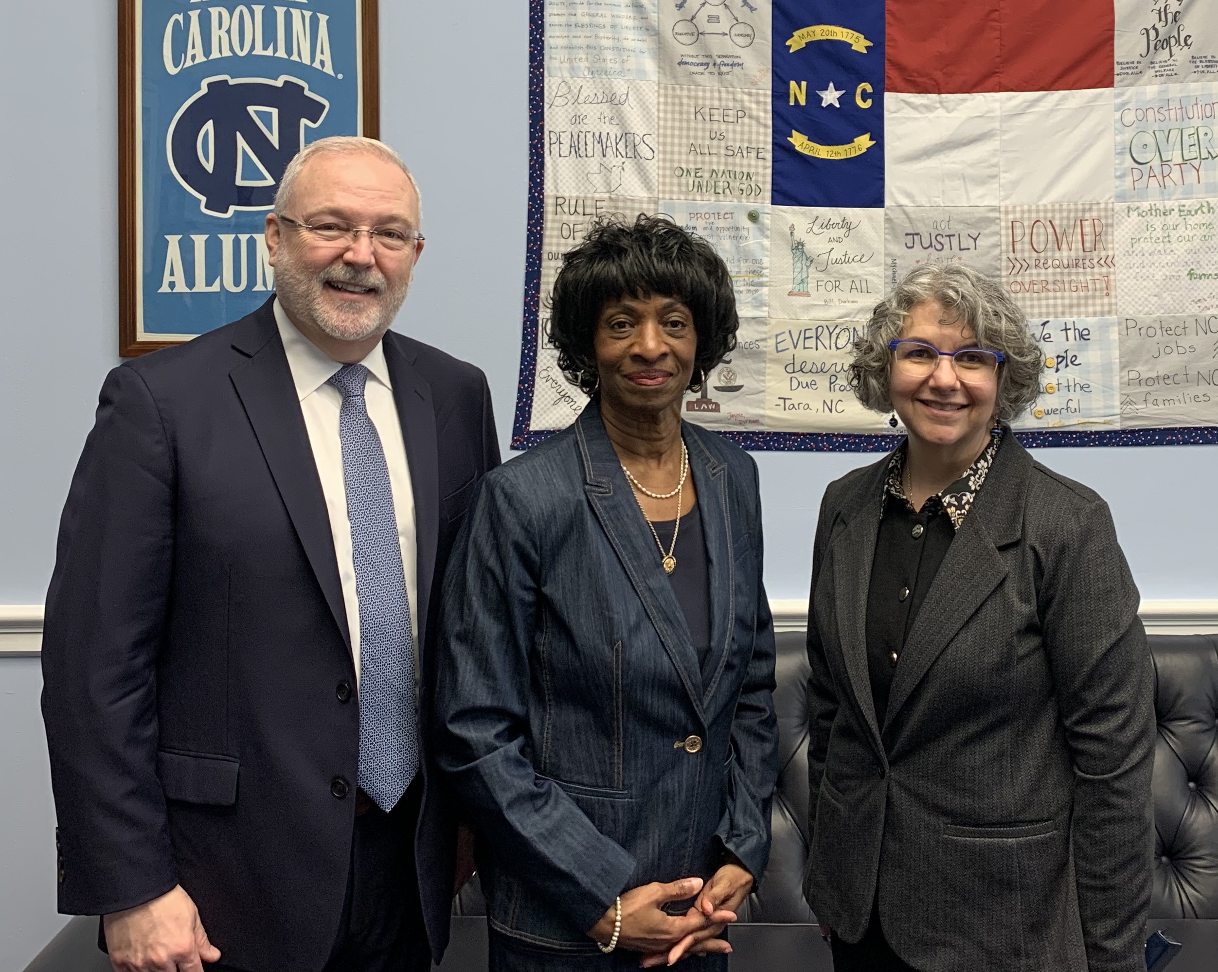 Michael Relf, Valerie Foushee, and Terry McDonnell stand in Rep. Foushee's Office in front of a North Carolina flag.