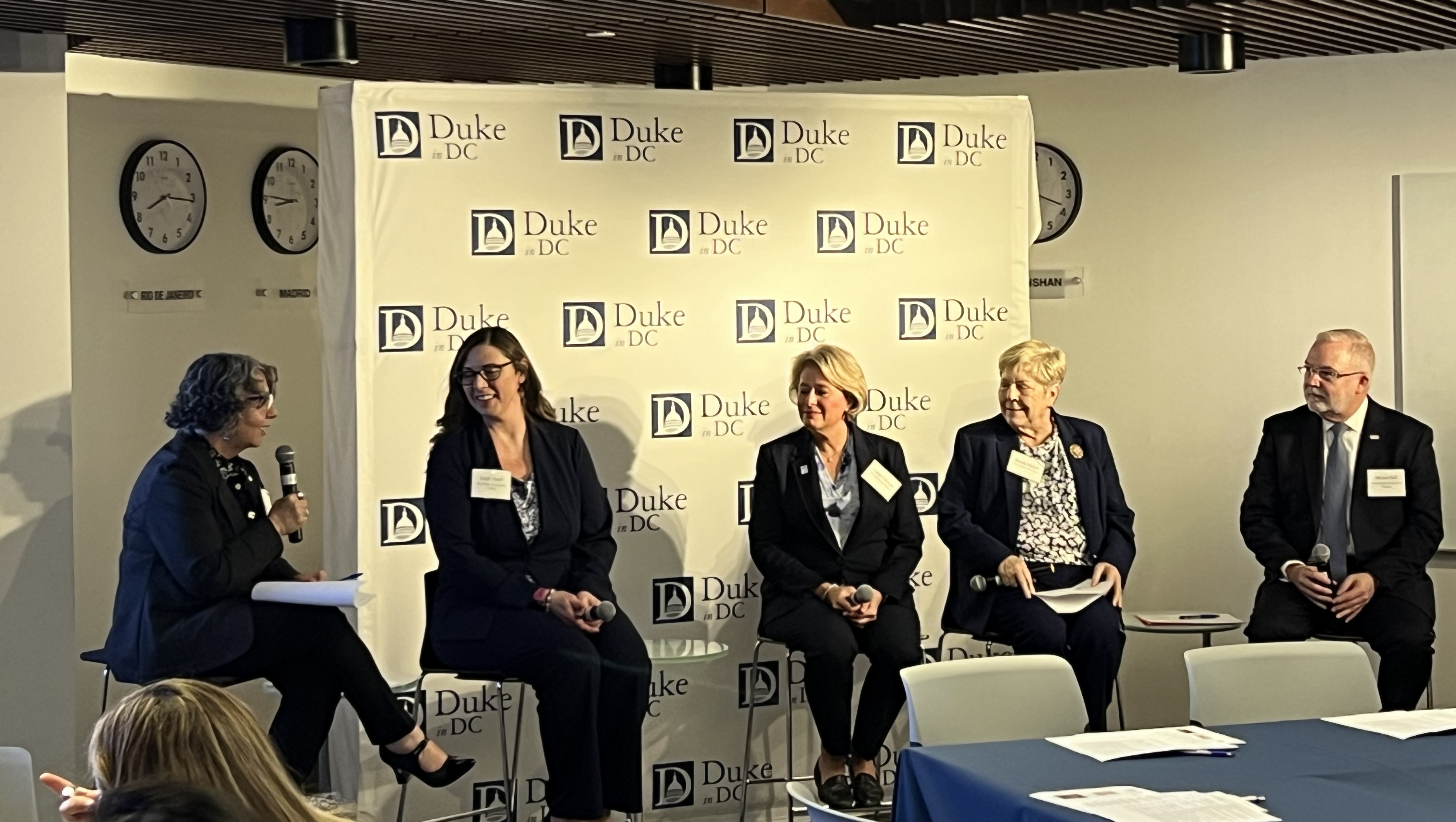 Terry McDonnell and Michael Relf sit at either end of a panel seated in front of a Duke in DC banner.