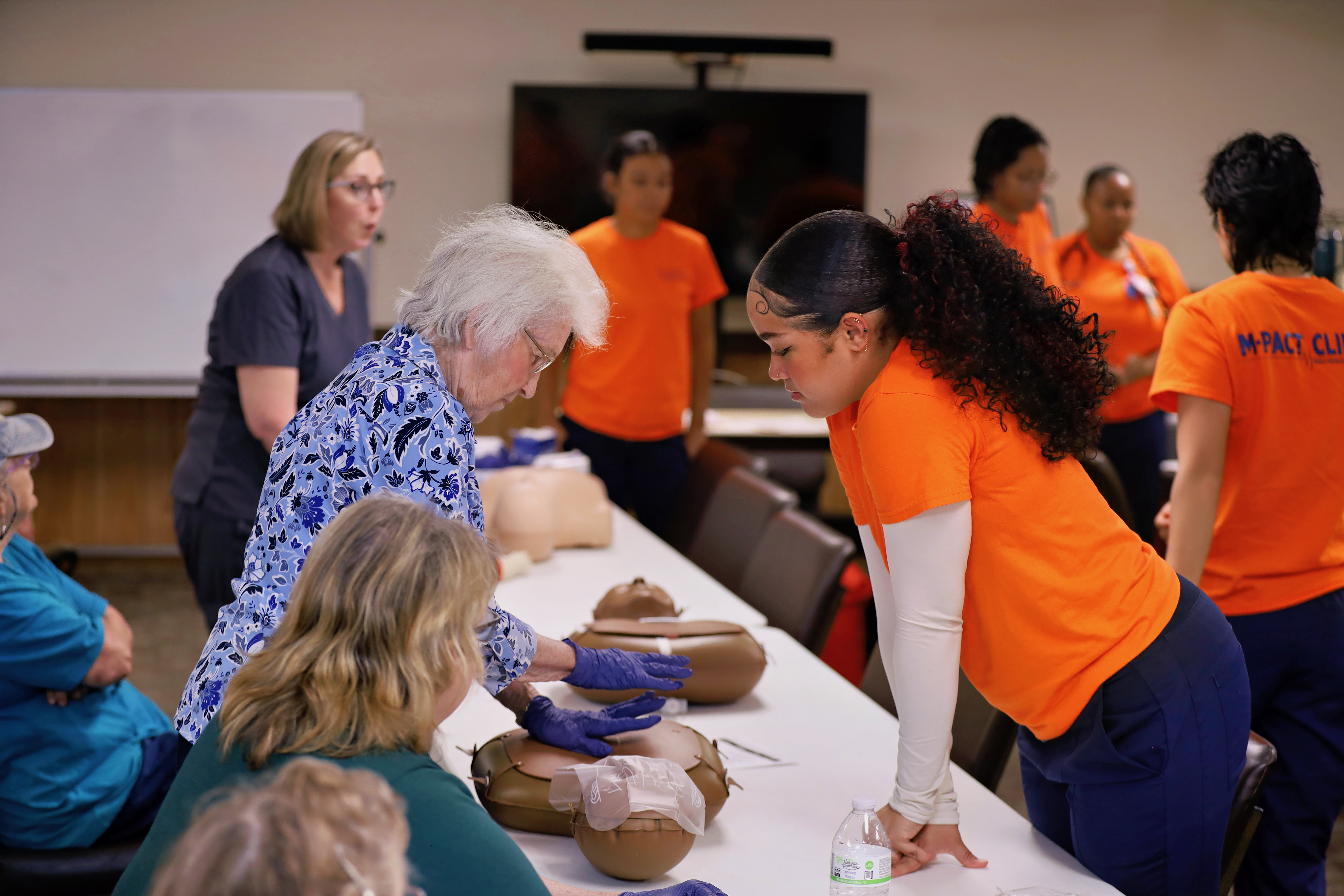 Duke Nursing student in orange shirt watches senior practicing CPR