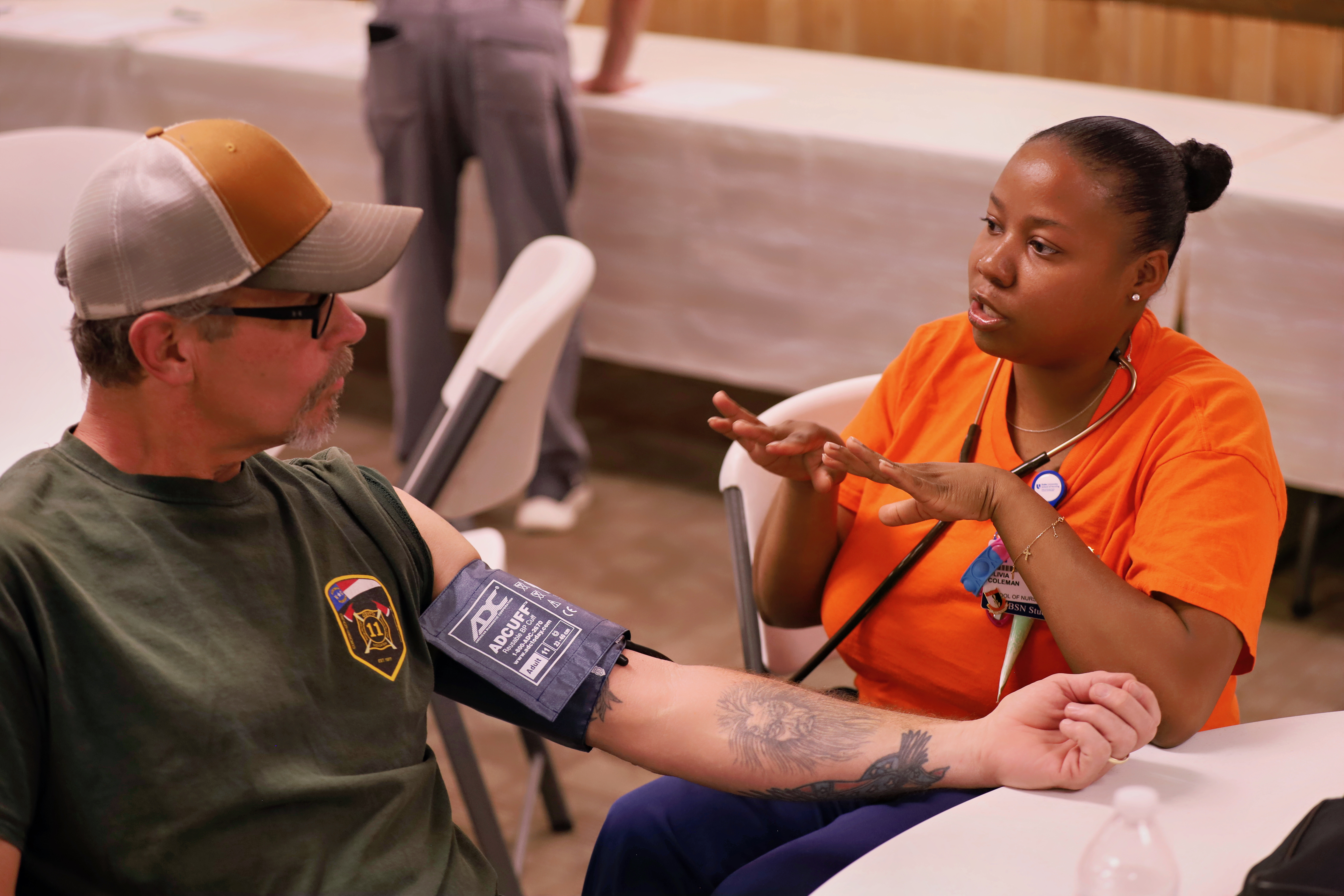 A School of Nursing student administers a blood pressure screening to a man wearing a baseball cap