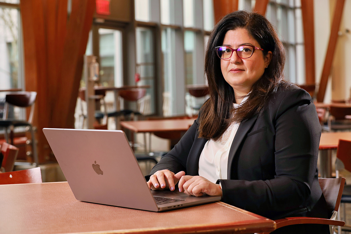 Dr. Mariam Kayle sits at a table in a large atrium. She has a laptop in front of her.