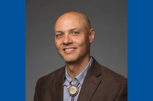 Seminar speaker, Dr. Ryan Emanuel, smiling, wearing a suit jacket, gingham collared shirt, and bolo tie