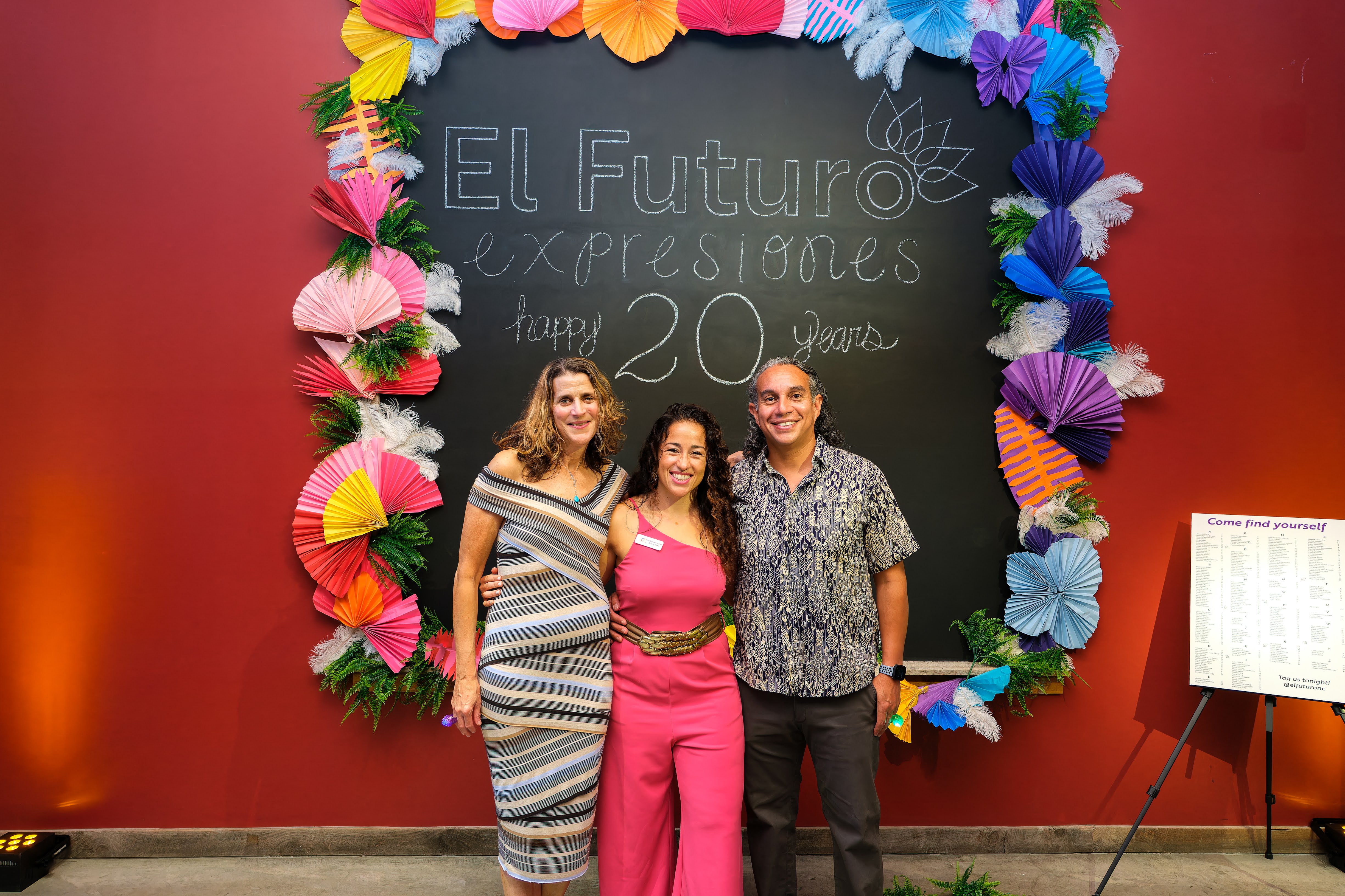 Three people in front of blackboard that reads, "El Futuro expresiones happy 20 years"