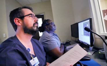 A male Duke University Nursing MSN Health Informatics Student sits infront of health analytics on a monitor beside a female health informatics nursing student.