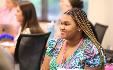 A young female Duke MSN Pediatric Primary Care student smiling and sitting in a classroom.