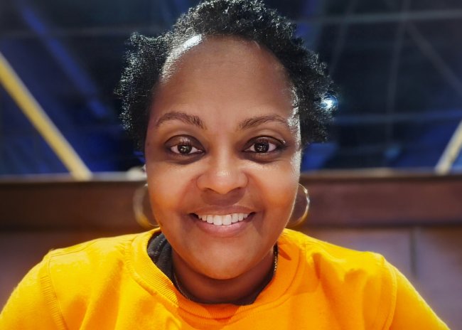 A woman smiles for the camera while wearing a yellow shirt.