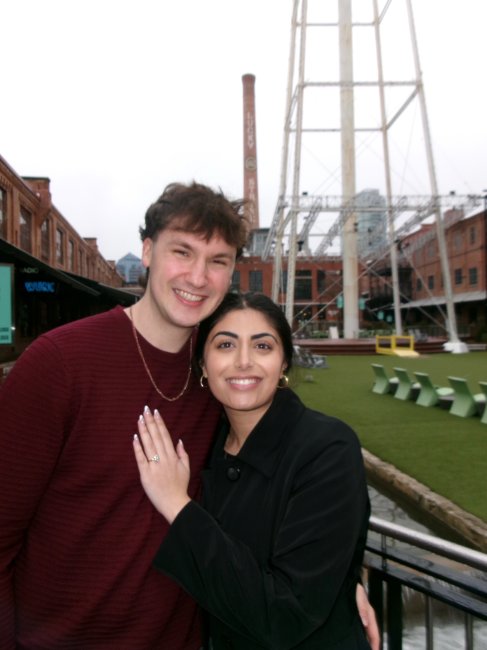 Two people pose in the inner courtyard of the American Tobacco Campus in downtown Durham, NC. The iconic white water tower is in the background. It appears to be an engagement photo.