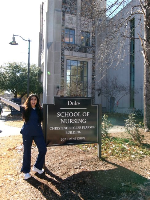 A person poses outdoors next to a sign for Duke University School of Nursing.