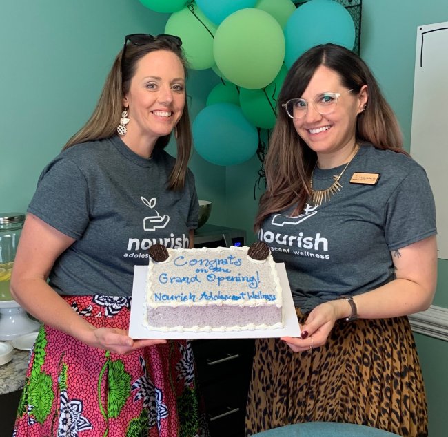 two women holding cake at grand opening 